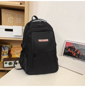 Detailed view of black nylon backpack with durable top handle and brand patch on desk