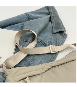 Detail of light khaki nylon tote bag featuring wide adjustable strap on denim background