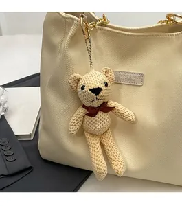 Detail of a handmade crocheted bear charm with a brown bow on a canvas tote bag