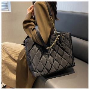 Close-up of black quilted nylon tote bag with golden chain and faux leather strap
