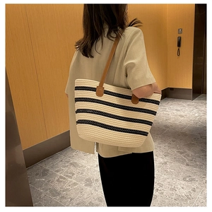 Detailed view of woven striped tote bag with leather straps on a model's shoulder