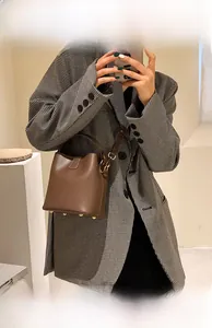 Detailed view of a brown bucket bag with metal feet and a detachable shoulder strap