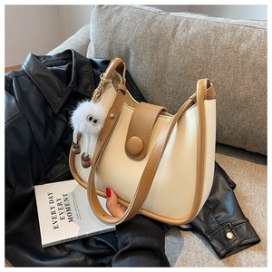 Detail of minimalist cream half-moon bag with brown trim and cute fuzzy keychain
