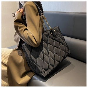 Detail of black quilted nylon tote bag featuring gold chain strap and padded texture