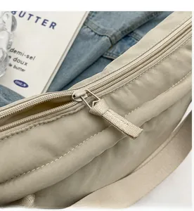 Close-up of smooth metal zipper and nylon fabric detail on beige shoulder bag
