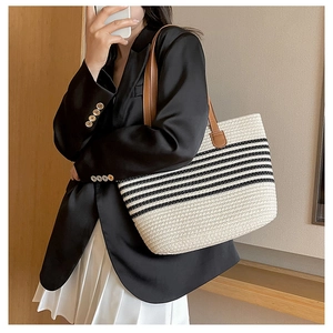 Close-up of woven straw tote bag featuring black stripes and brown leather shoulder straps