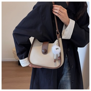 Detail of minimalist bucket bag showing coffee trim, fold-over strap, and plush charm