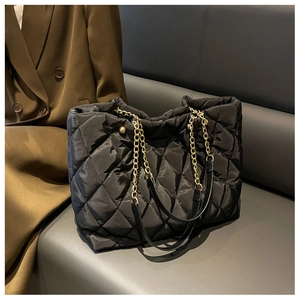 Macro shot of black quilted nylon texture with luxury gold chain handle on tote bag