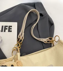 Detail of beige corduroy tote strap with golden chain links and teddy bear charm