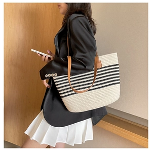 Close-up detail of large woven straw tote bag with striped pattern and brown leather handles
