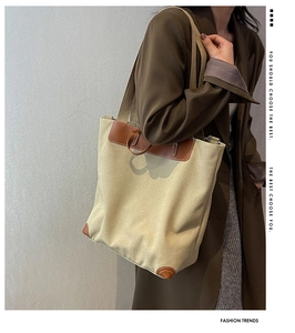 Side view of beige canvas tote bag with brown faux leather trim worn by a model