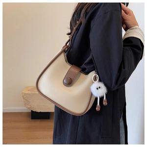 Detail view of a retro cream and brown shoulder bag with a cute fuzzy monster charm