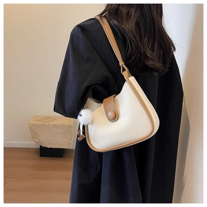 Detail of cream and brown shoulder bag with plush charm on a minimalist model
