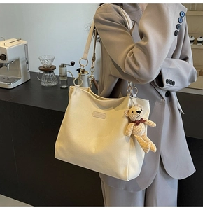 Detail of beige canvas tote bag with chain strap and cute knitted bear charm accessory