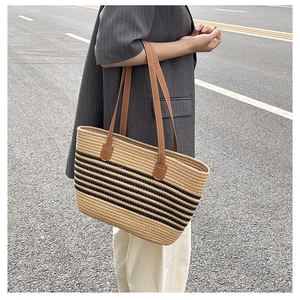 Detail of hand-woven straw tote with black stripes and sturdy brown leather shoulder straps