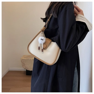 Detail of a minimalist two-tone half-moon shoulder bag with a plush charm accessory