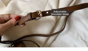 Detail of adjustable brown leather shoulder strap with gold buckle on white fabric