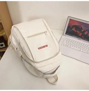 Close-up of white minimalist backpack with front zipper and red RUIKEDA logo on desk