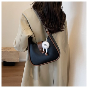 Detail of a black and brown crossbody bag with a cute white plush monster charm