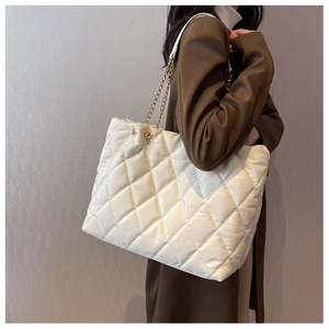 Quilted white tote bag with gold chain strap shown on model shoulder for daily commute