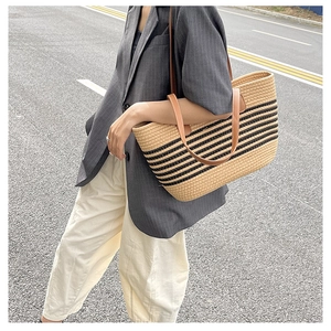 Close-up of woven straw tote bag with black stripes and brown leather handles