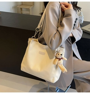 Close-up of cream canvas tote bag featuring a leather chain strap and brown teddy bear charm