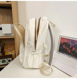 Detail view of the multi-layer interior and side pocket of a cream white backpack