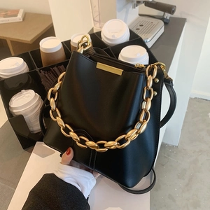 Elegante borsa a secchiello in pelle nera con catena dorata in un caffè