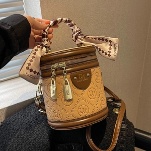 Braune Beuteltasche mit Tuch am Griff und Monogramm-Print, von einem Model präsentiert