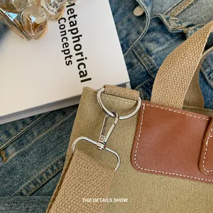 Detalle del bolso de lona con cierre giratorio de metal plateado y ribete de cuero marrón