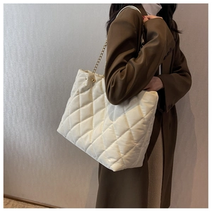 Quilted tote bag with golden chain strap worn over the shoulder on a brown blazer