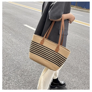 Detail of beige straw tote bag with black stripes and brown faux leather shoulder strap