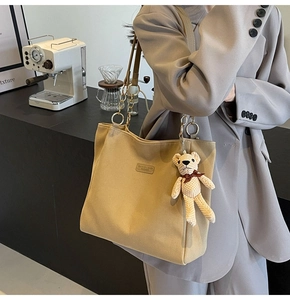 Canvas tote bag with metal chain strap and cute teddy bear charm in a cafe setting