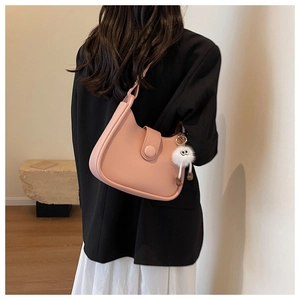 Detail of pink hobo bucket bag with plush charm on a model in a minimalist setting