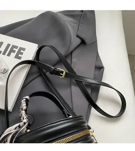 Détail du sac bandoulière noir rond avec poignée en foulard à rayures et détails dorés