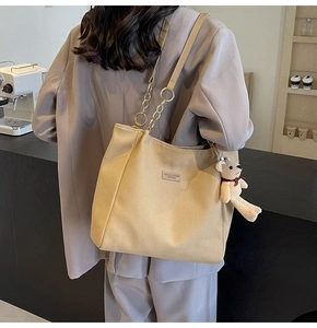Detail of khaki canvas tote bag with chain strap and teddy bear charm on model