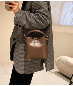 Close-up of a brown leather bucket bag showing the brand logo and adjustable shoulder strap