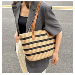 Detail of a large woven straw tote bag with black stripes and brown leather straps