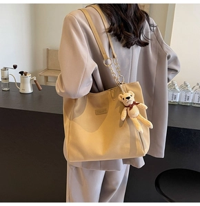 Detail of beige canvas tote bag with bear charm and leather logo in a cozy cafe setting