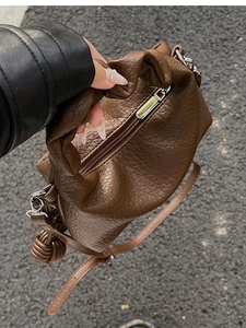 Détail d'un sac à main marron plissé avec fermeture éclair argentée et pendentif en cuir