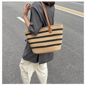 Detailed side view of a large woven tote bag with black stripes and brown leather straps