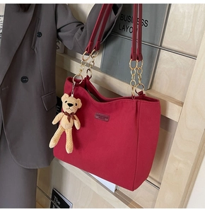 Detail of red tote bag featuring a metal chain strap and a cute bear plush pendant
