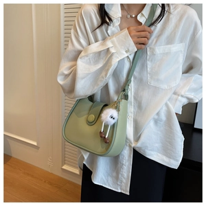 Detail of light green crescent shoulder bag with plush charm and adjustable strap