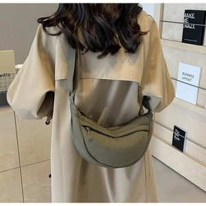 Detail view of military green nylon crescent bag worn crossbody over a khaki trench coat
