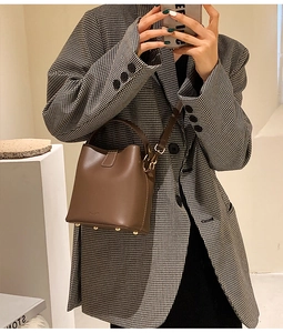Close-up of brown bucket bag showing smooth leather texture and gold metal feet on base