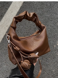 Détail d'un sac en cuir marron chocolat avec poignée plissée et charmes à nœuds uniques