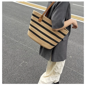 Detail of hand-woven straw tote bag with black stripes and reinforced faux leather handles