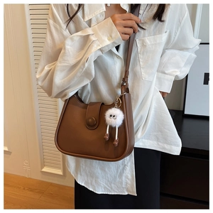 Detail of a brown semi-circular shoulder bag featuring a cute white plush monster charm