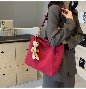 Detail of red canvas tote bag featuring gold chain strap and cute plush bear charm