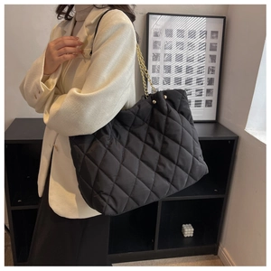Detail of black quilted nylon tote bag with golden chain strap on model's shoulder